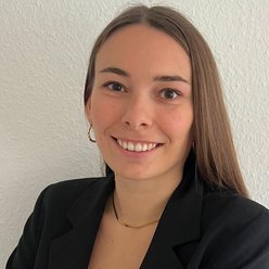 Person mit langen, dunklen Haaren, Shirt weiß und Blazer dunkel