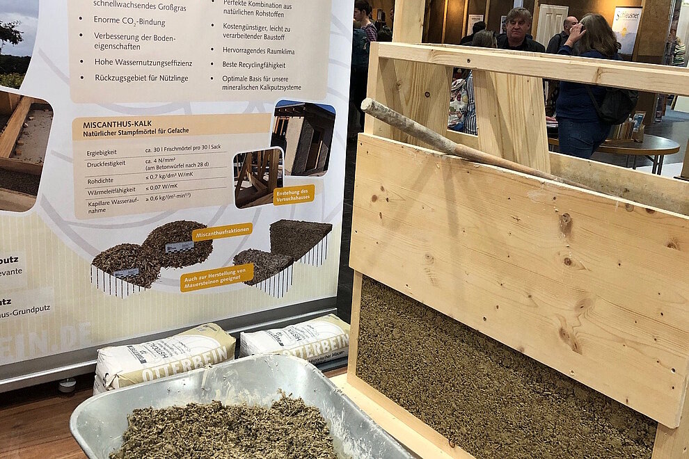 Stand auf einer Veranstaltung zum Rohstoff Miscanthus, Schubkarre mit Rohstoff gefüllt