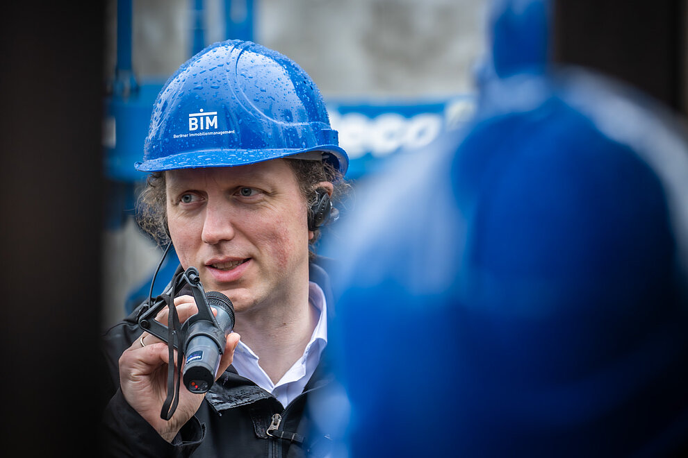 Person mit einem blauen Helm und Mikrofon in der Hand