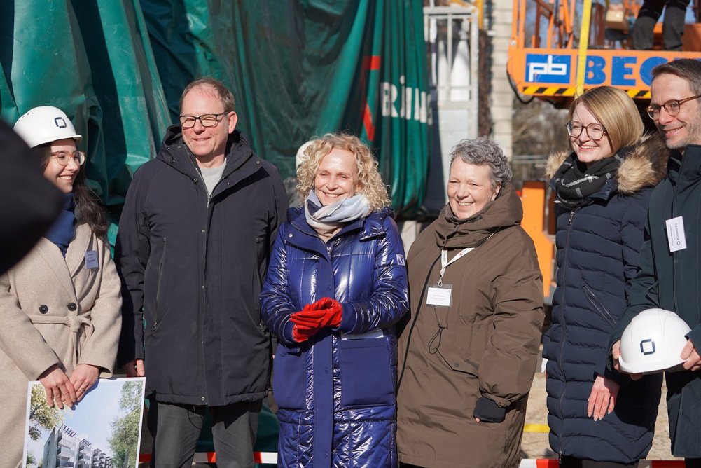 Personen in warmer Kleidung stehen nebeneinander auf einer Baustelle.
