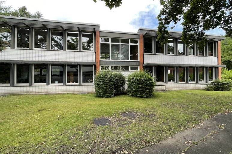 Schulgebäude zweigeschossig, davor Rasenfläche mit zwei Sträuchern