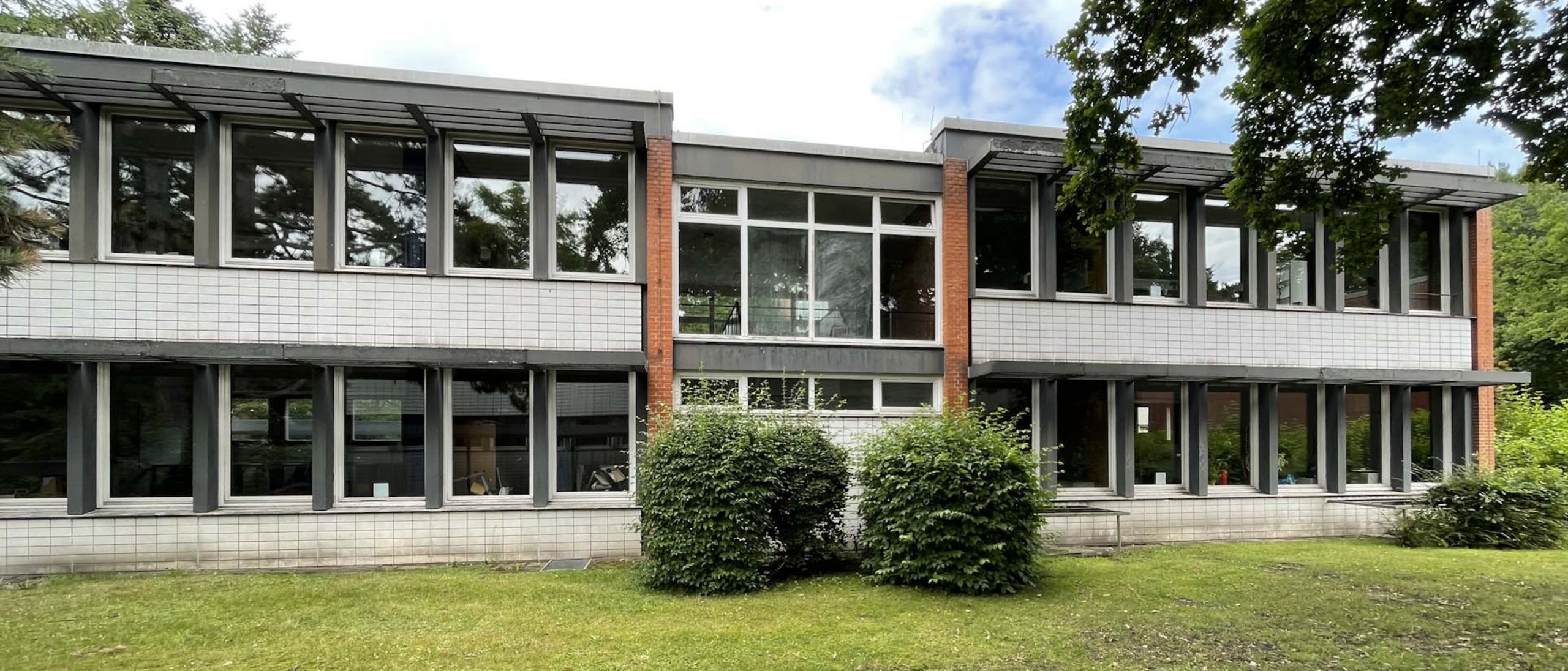 Schulgebäude zweigeschossig, davor Rasenfläche mit zwei Sträuchern