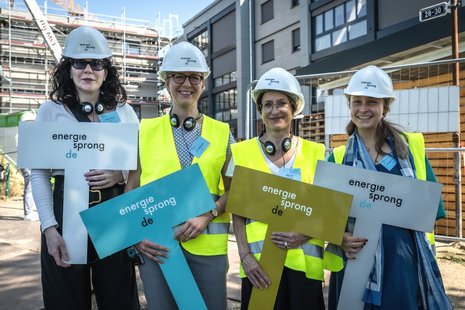 Vier weibliche Personen stehen nebeneinander, auf den Köpfen weiße Bauhelme, in den Händen jeweils ein Schild mit der Aufschrift: energiesprong.de