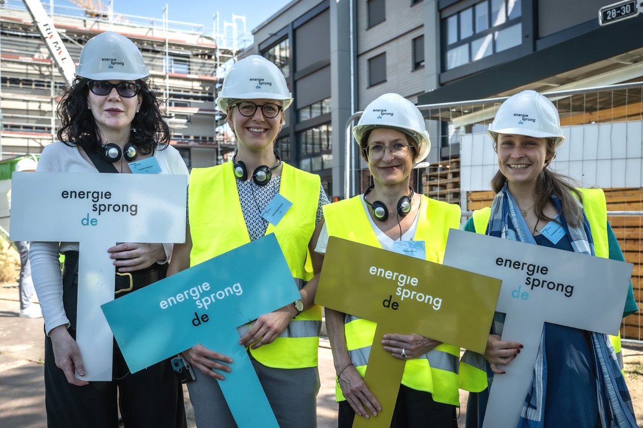 Vier weibliche Personen stehen nebeneinander, auf den Köpfen weiße Bauhelme, in den Händen jeweils ein Schild mit der Aufschrift: energiesprong.de