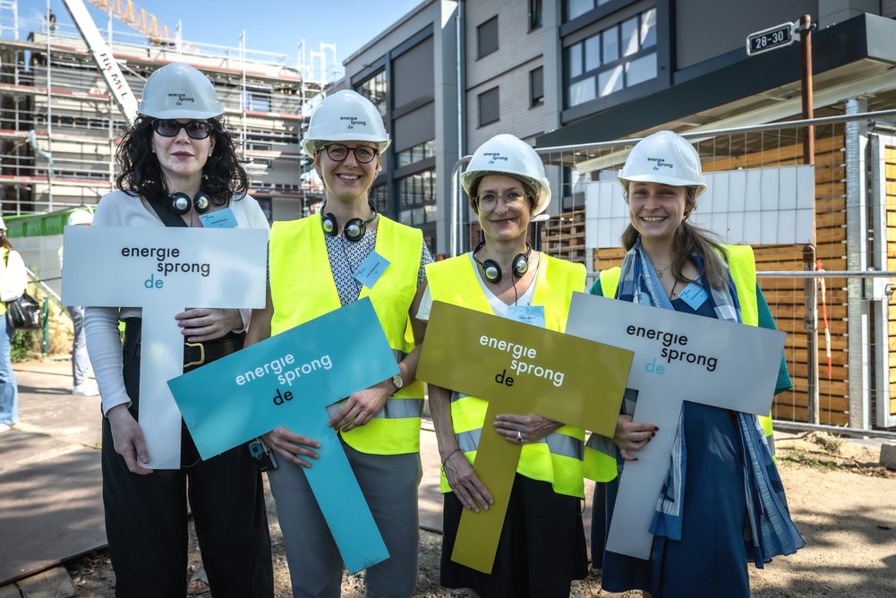 Vier weibliche Personen stehen nebeneinander, auf den Köpfen weiße Bauhelme, in den Händen jeweils ein Schild mit der Aufschrift: energiesprong.de