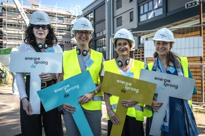 Vier weibliche Personen stehen nebeneinander, auf den Köpfen weiße Bauhelme, in den Händen jeweils ein Schild mit der Aufschrift: energiesprong.de