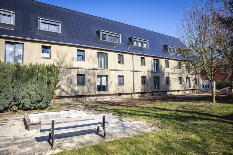 Mehrfamilienhaus zweigeschossig mit Solardach, davor Grünfläche mit Spielplatz, blauer wolkenloser Himmel